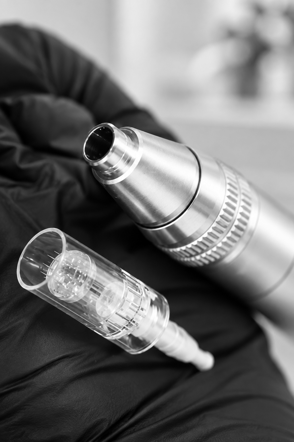 Gloved hands holding a microneedling pen, close-up in black and white