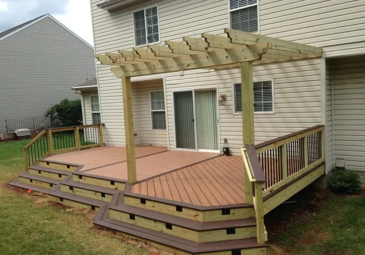 A wooden deck with stairs and a pergola in front of a house.
