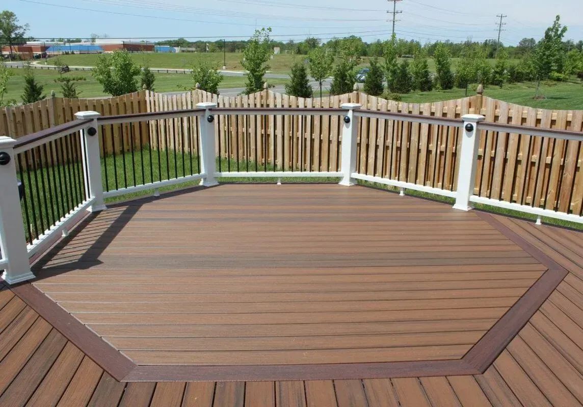 A wooden deck with a white railing and a wooden fence