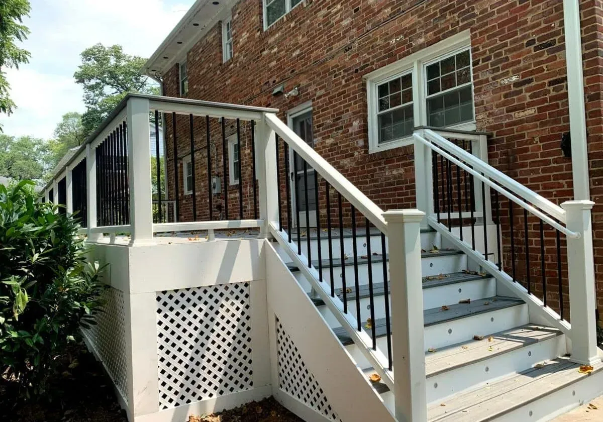 A white deck with stairs leading up to a brick house
