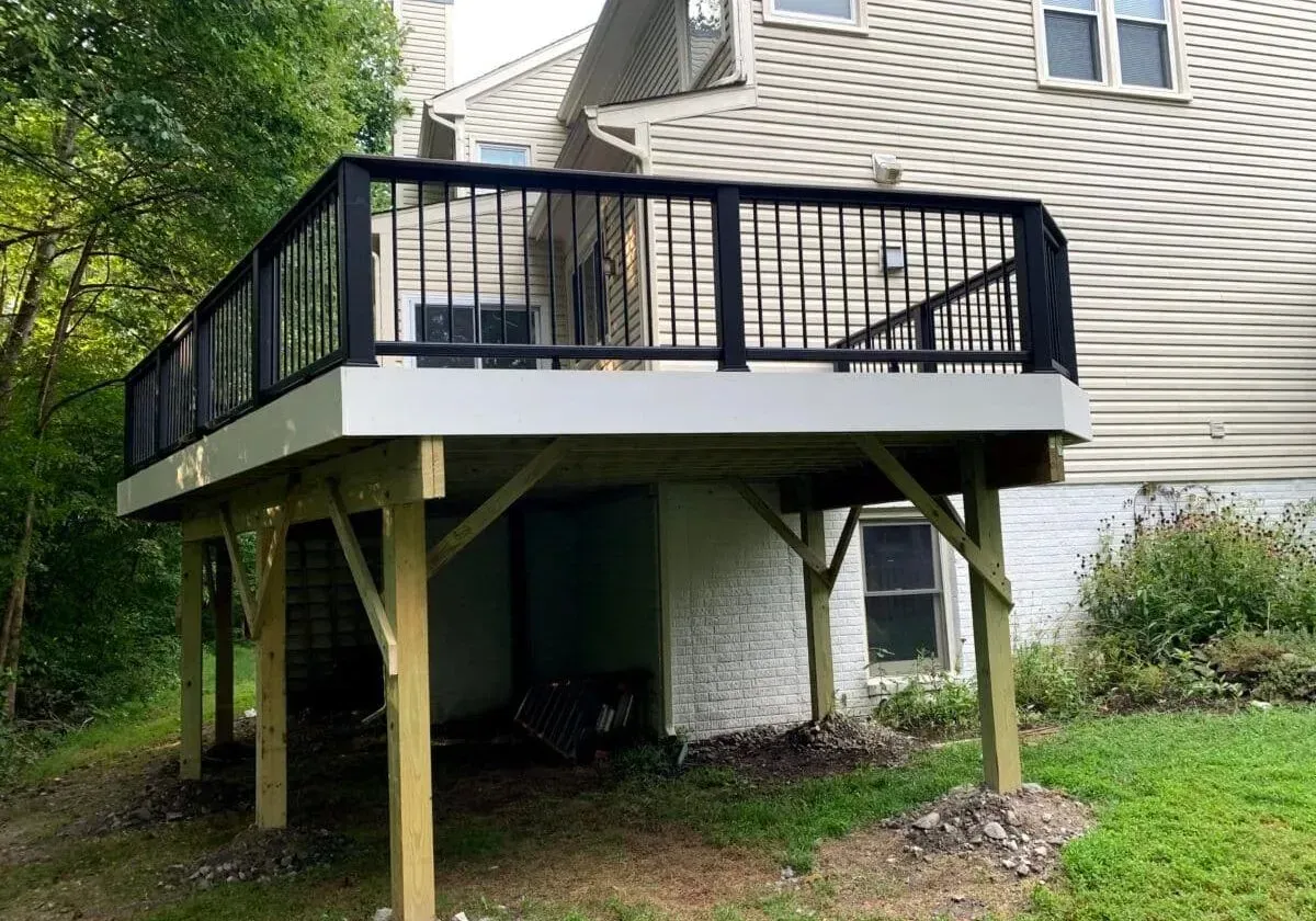 A wooden deck with a black railing is in front of a house.