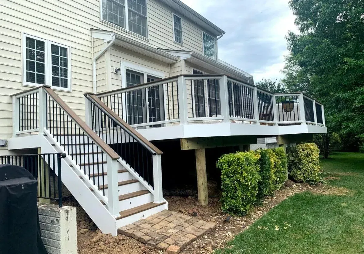 A large deck with stairs leading up to it is in the backyard of a house.