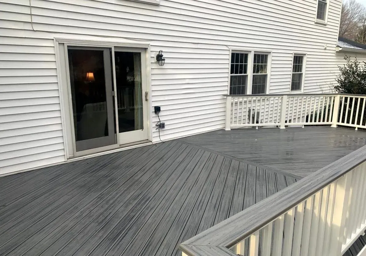 A large deck with a white house in the background and a sliding glass door.