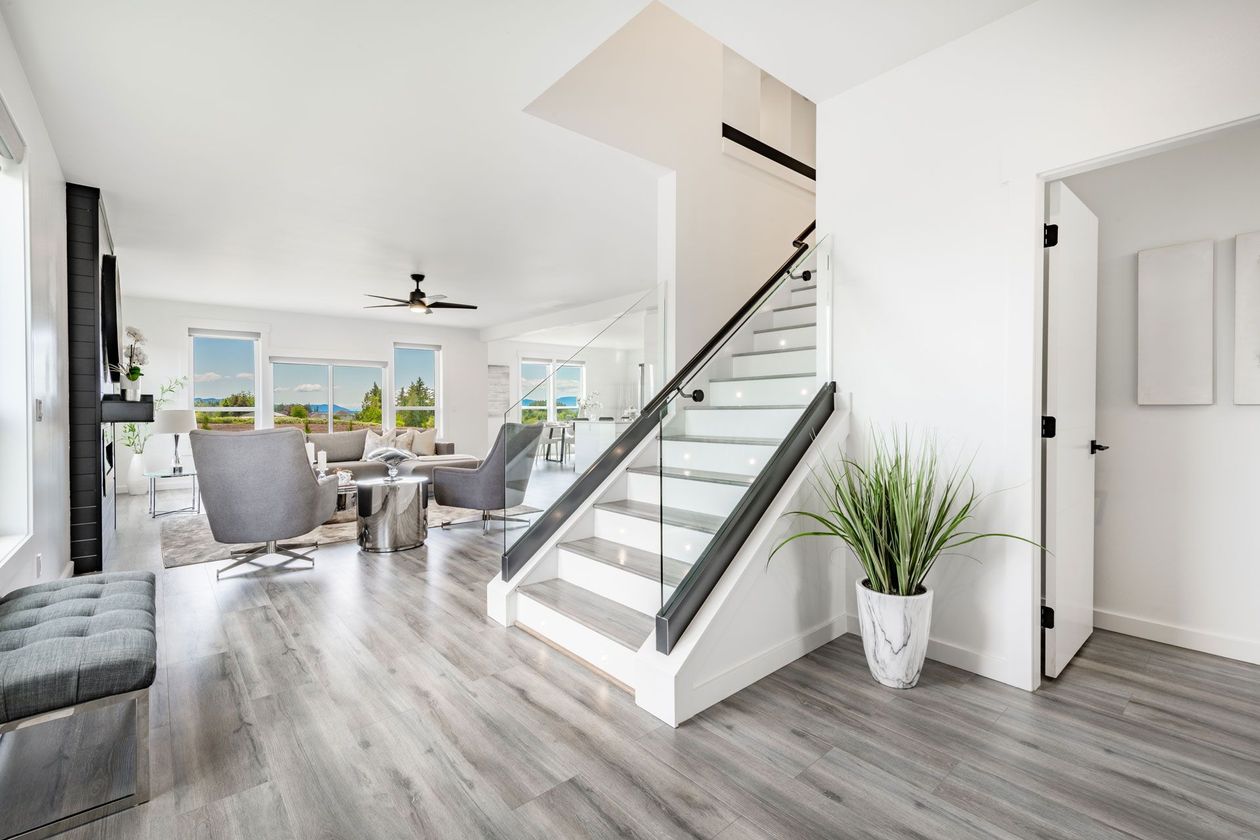 Bright, modern interior with staircase, gray flooring, and white walls. Includes a bench, plant, and view of the living area.