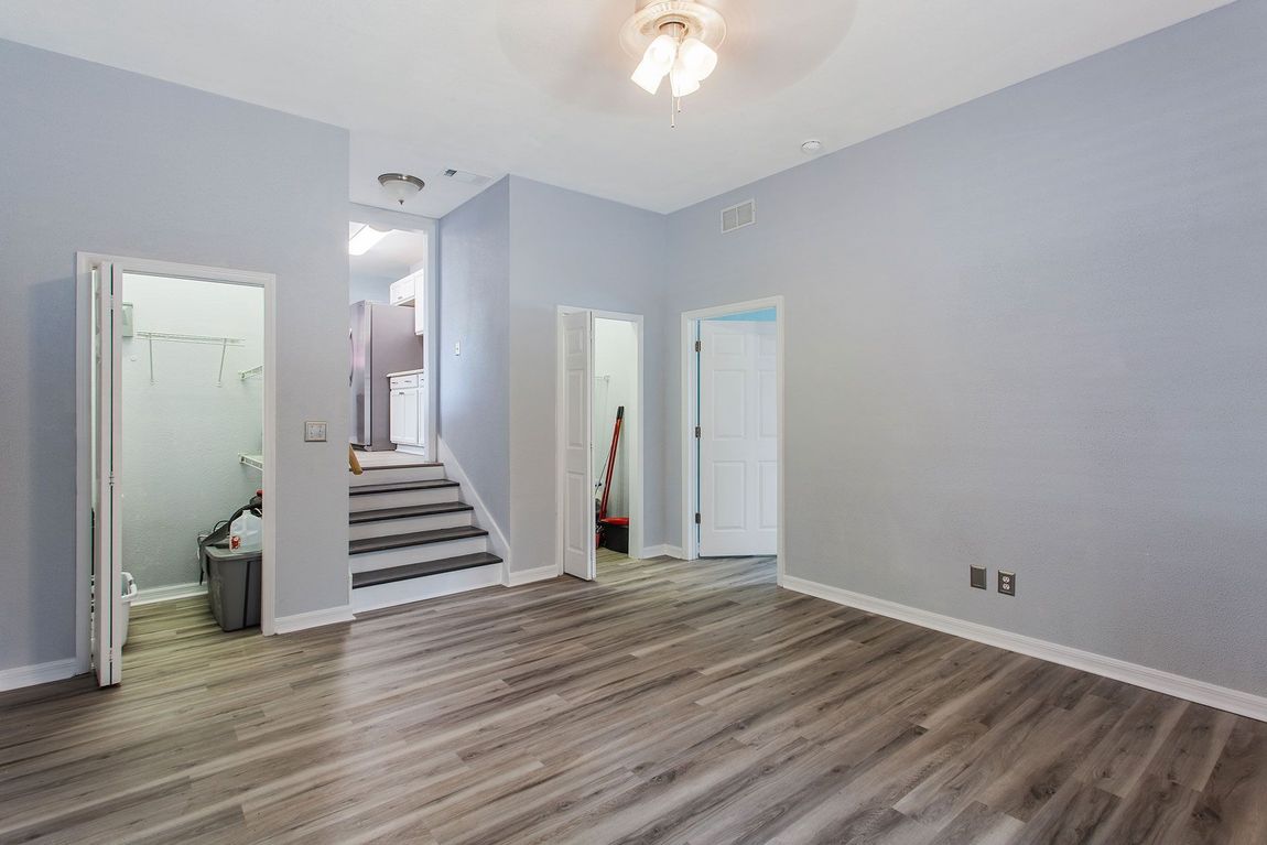 Empty room with light blue walls, gray wood-look floor, doorways, and stairs leading upwards.