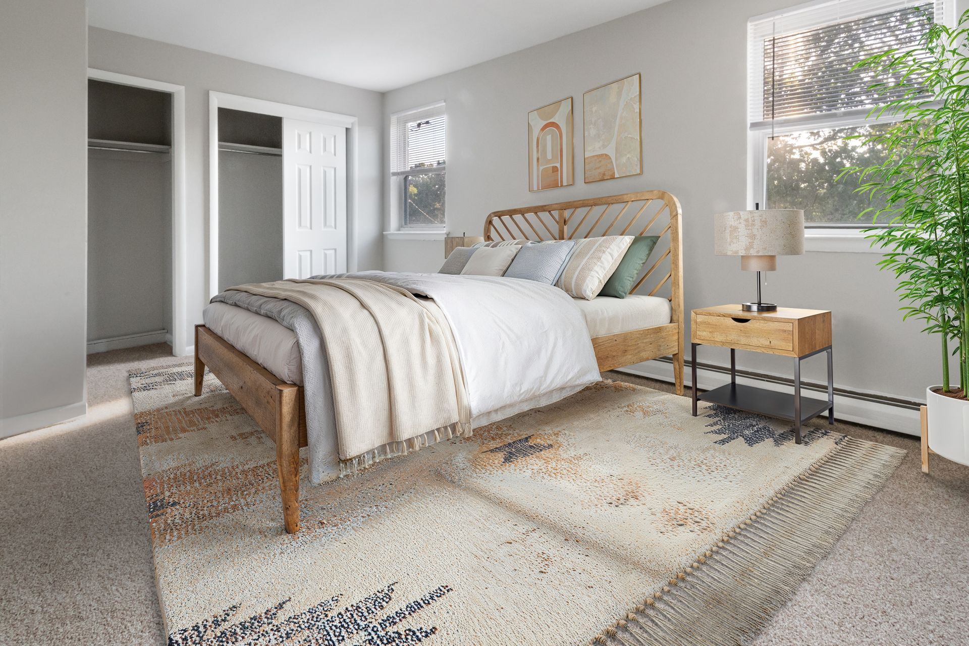 Bright bedroom with a wooden bed, light gray walls, open closet, and a bedside lamp by the window.