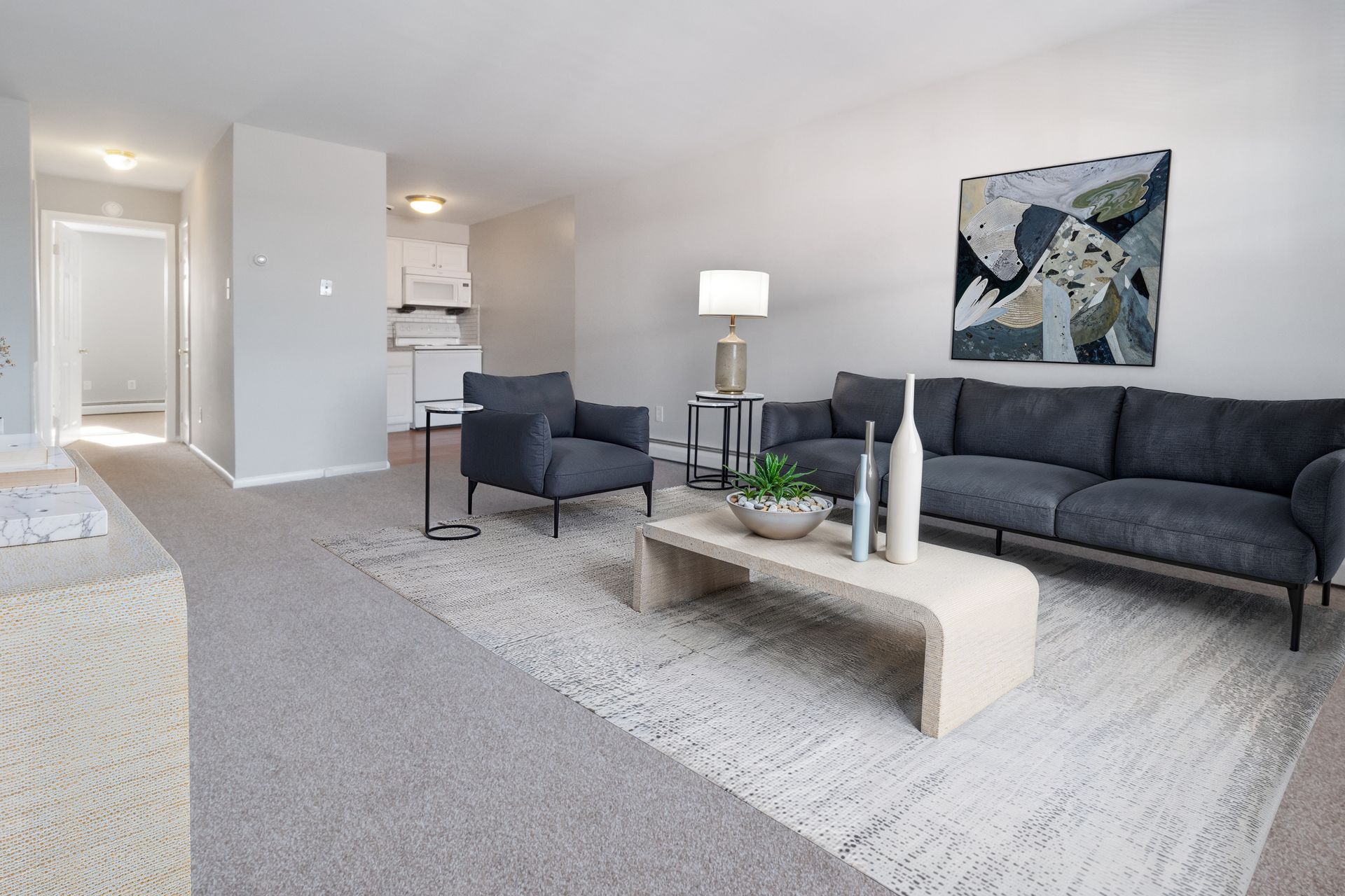 Bright modern living room with gray sofa, armchair, coffee table, floor lamp, and abstract wall art.