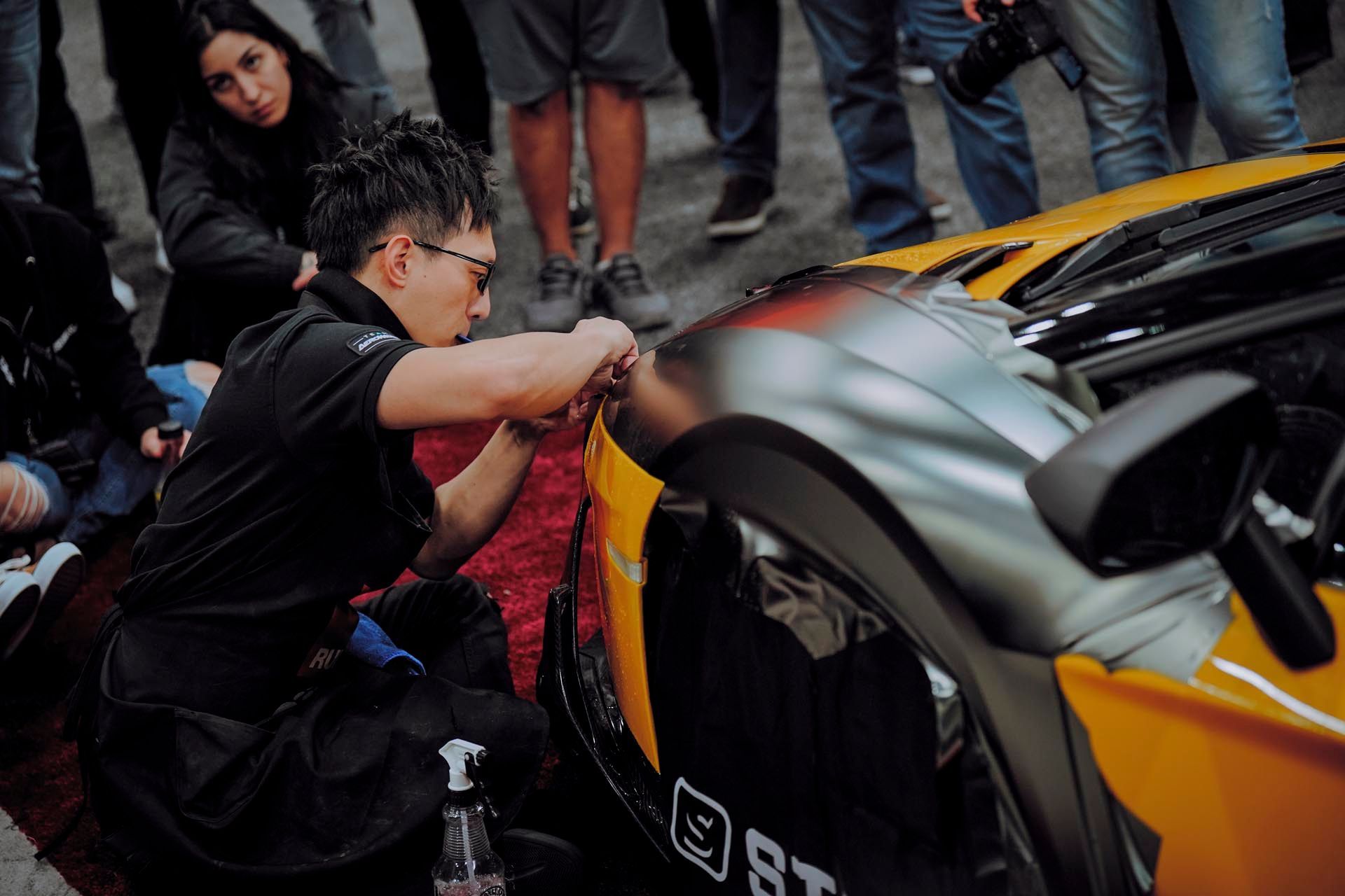 A man is working on the side of a yellow sports car.