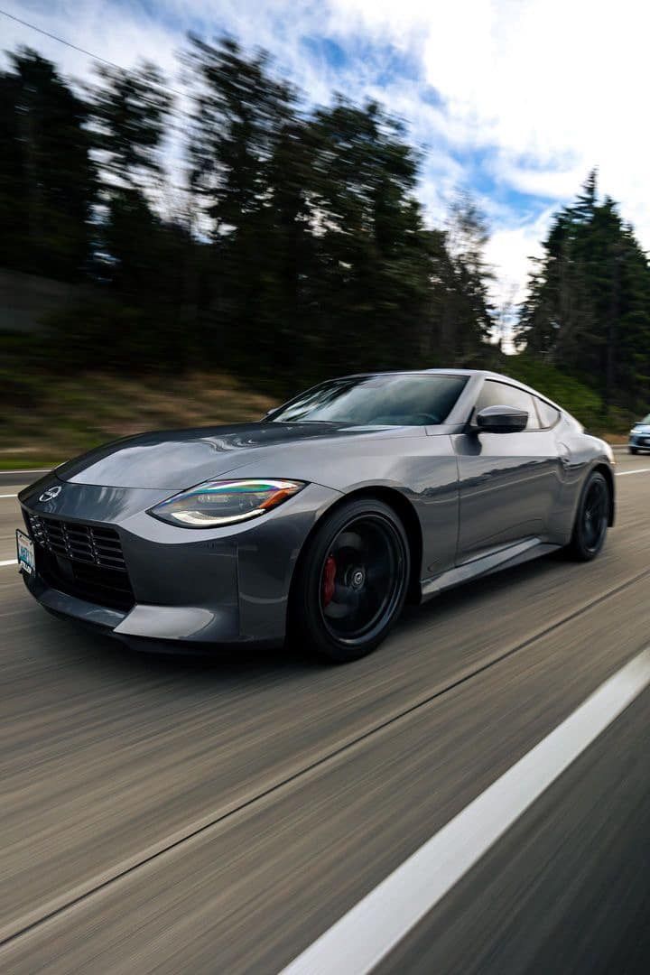 Gray sports car speeding on a highway with blurred background of trees and sky.
