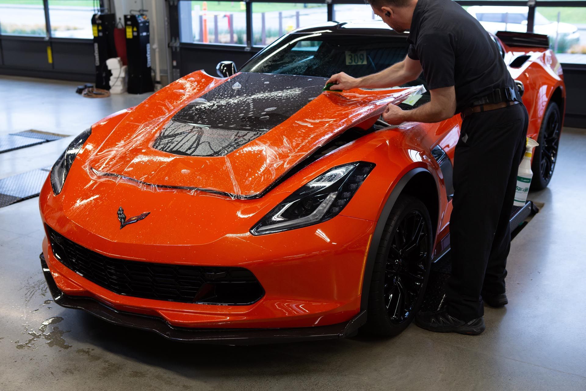 A man is covering the hood of an orange sports car in a garage.
