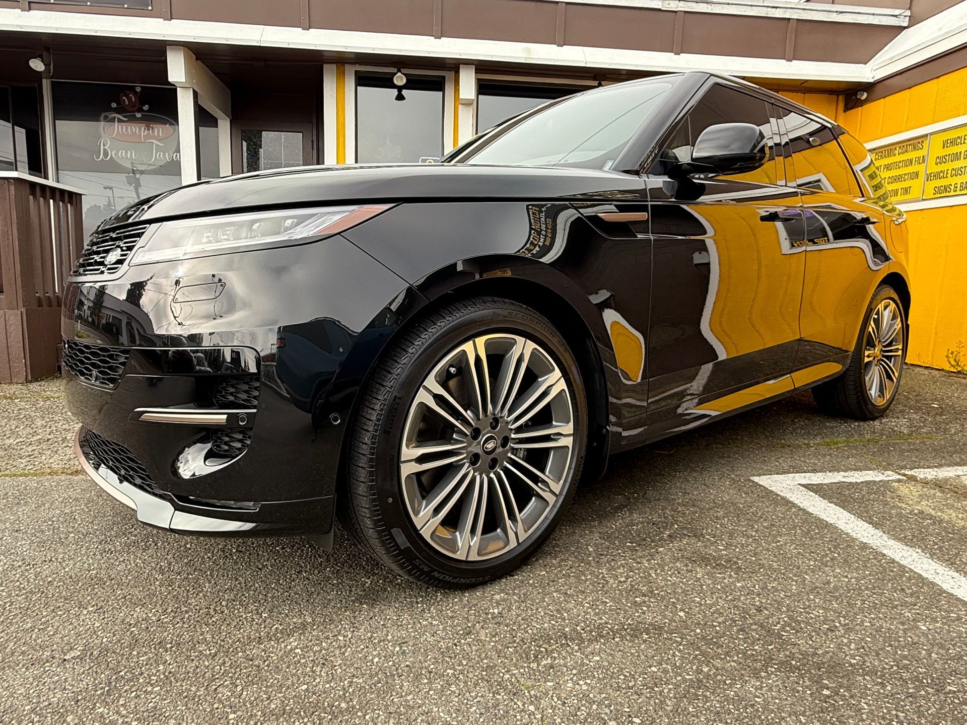 A black car is parked in a parking lot at the Top Notch Tint & Detail building.