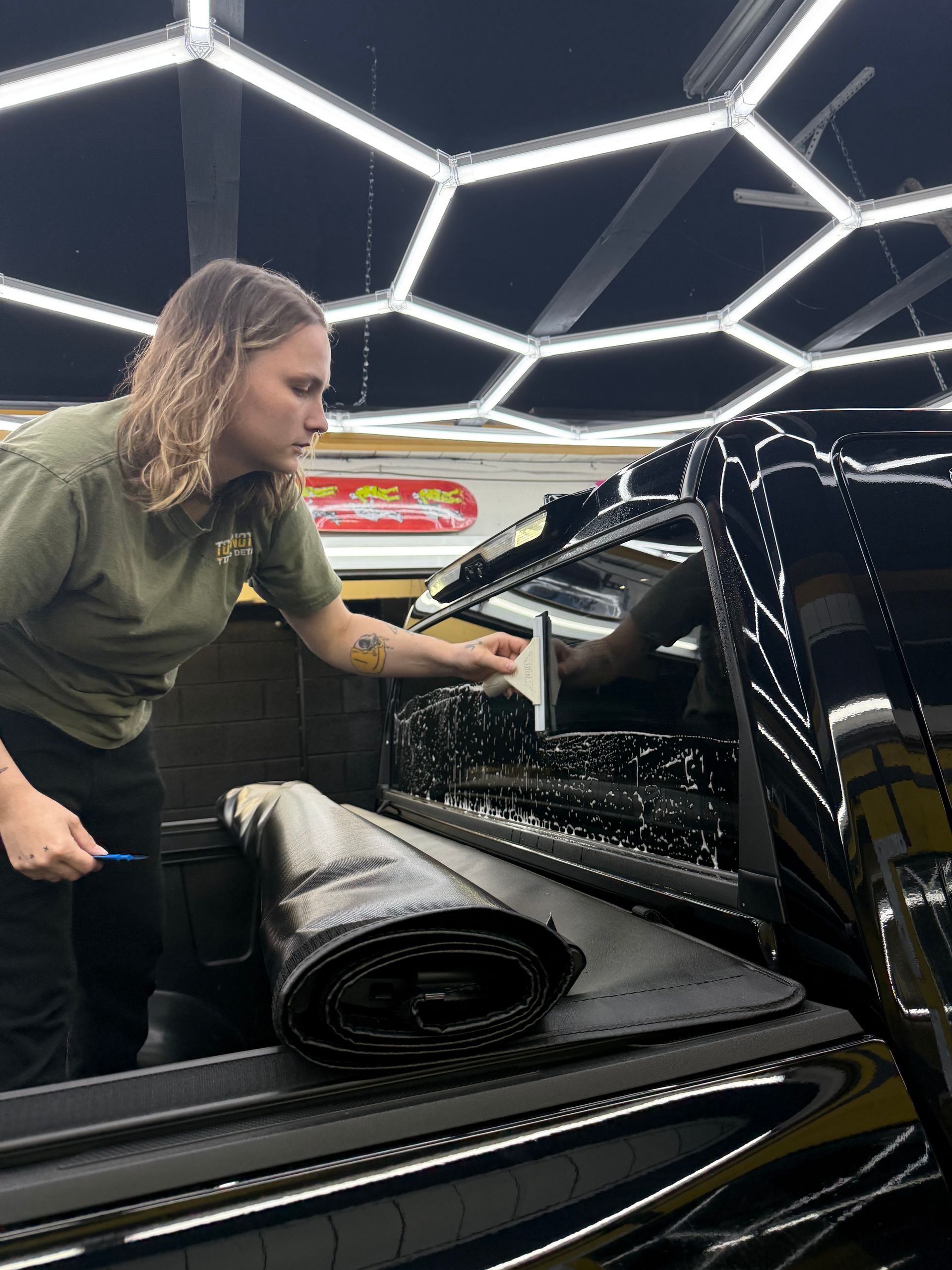 Person leaning into the rear cargo area of a shiny black vehicle under bright geometric ceiling lights