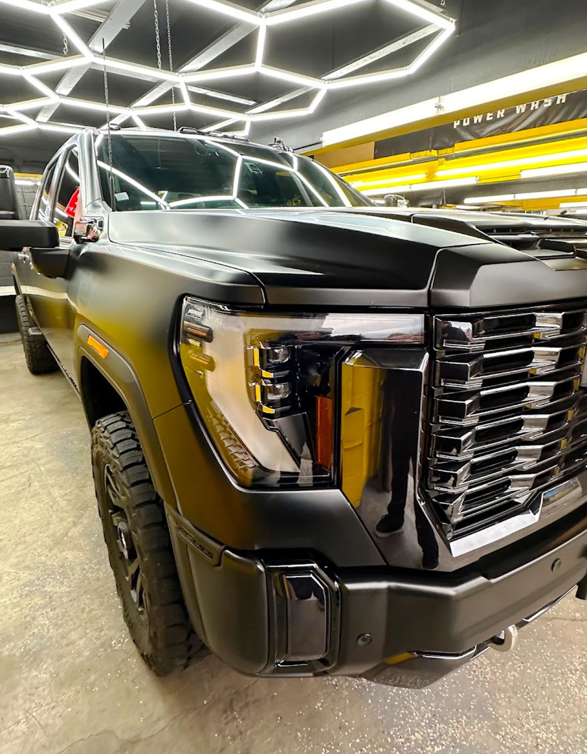 A black truck with a yellow grille is parked in a garage at Top Notch Tint & Detail .