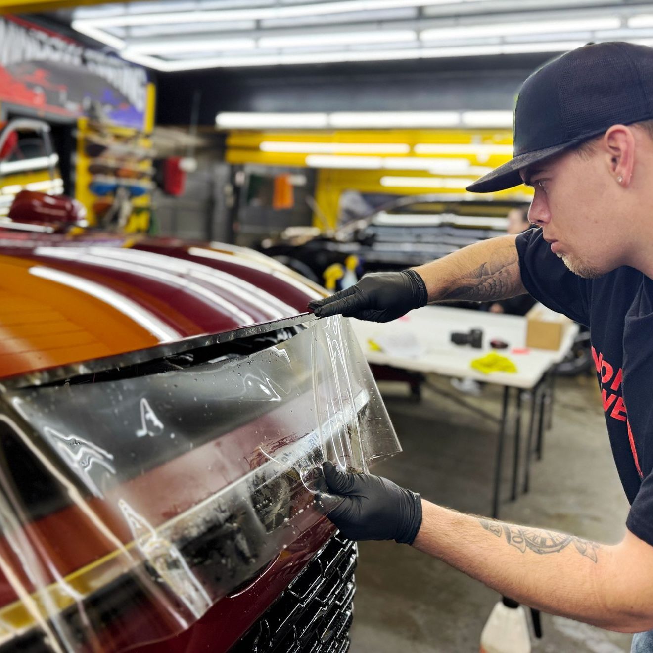 A man is applying a protective film to the hood of a car.