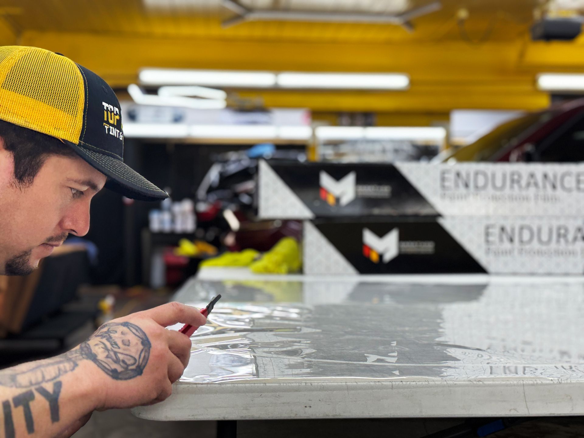 Worker inspecting a glossy white panel in a factory, with stacked Endurance boxes in the background