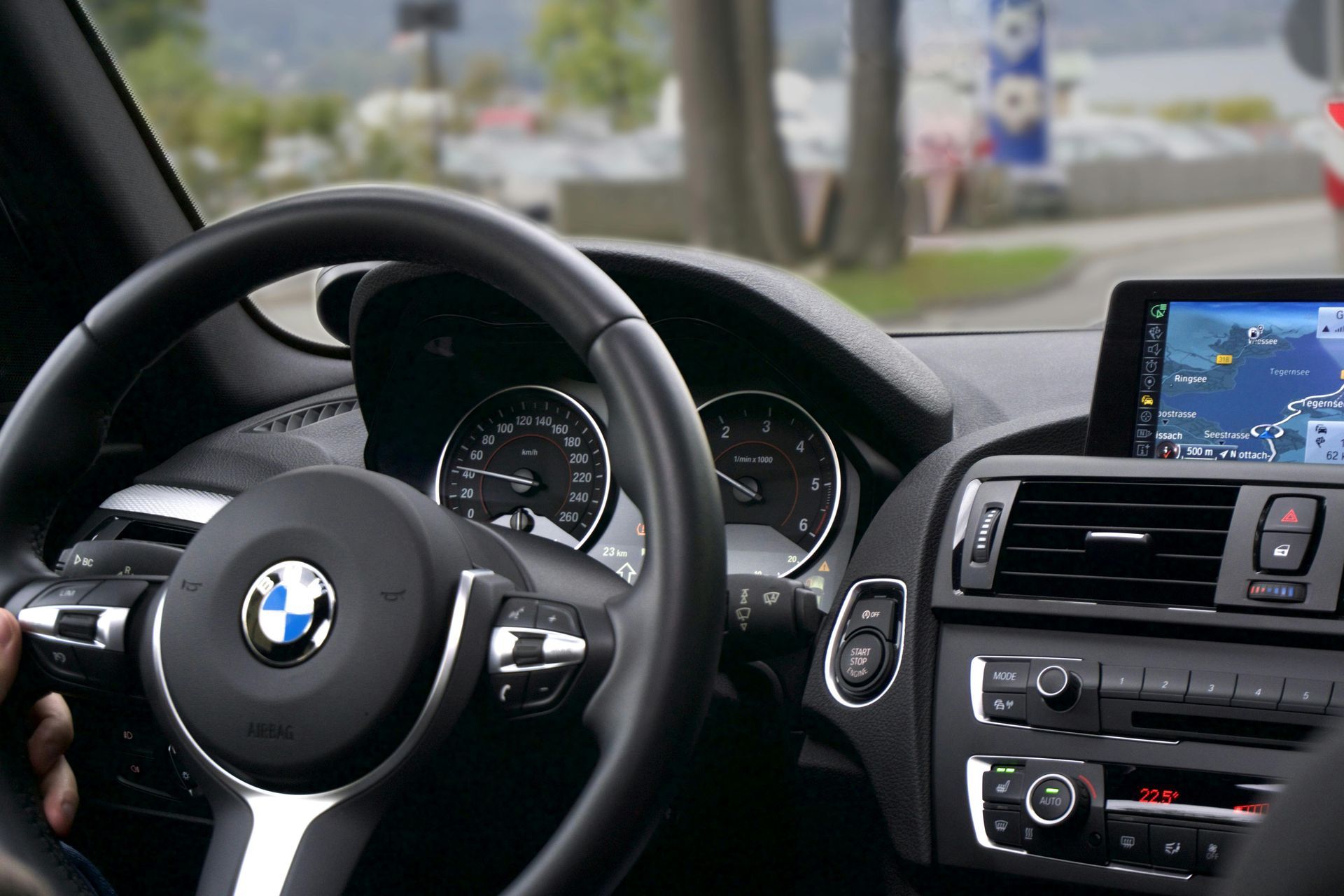 Interior view of a BMW car, showing steering wheel, dashboard with navigation screen, and the driver's hand on the wheel.