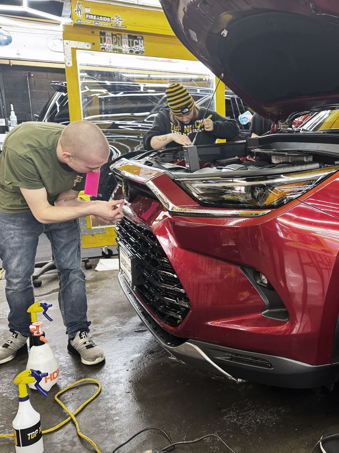 Two people are installing PPF on a red car in a garage at Top Notch Tint & Detail .