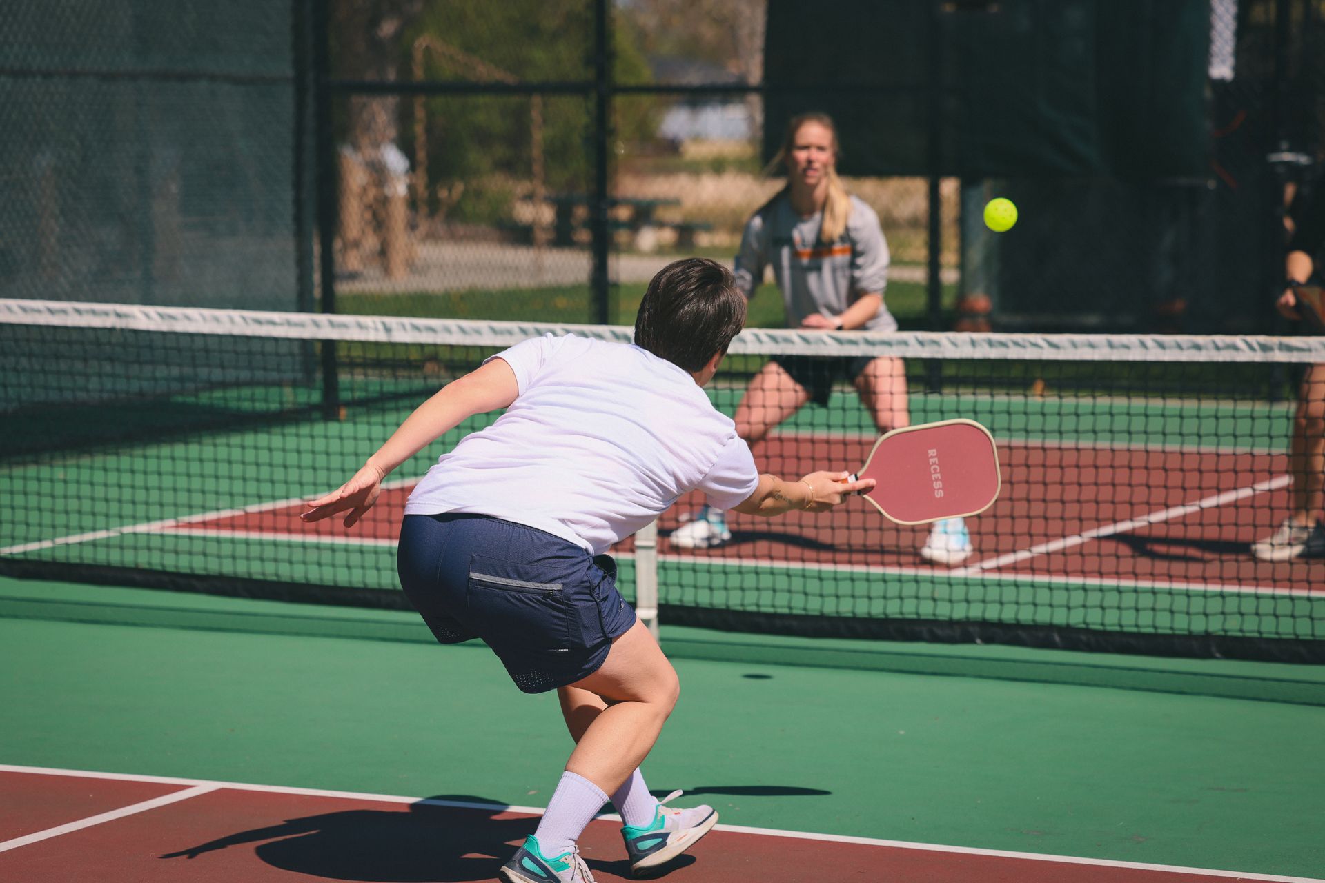 Two female pickleball players rally back and forth across the net.
