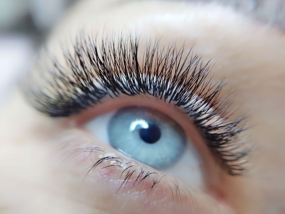 Primo piano di un occhio azzurro con lunghe ciglia scure e trucco leggero.
