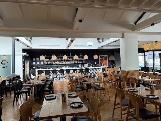 Modern restaurant interior with wooden tables, black chairs, and a long bar under pendant lights