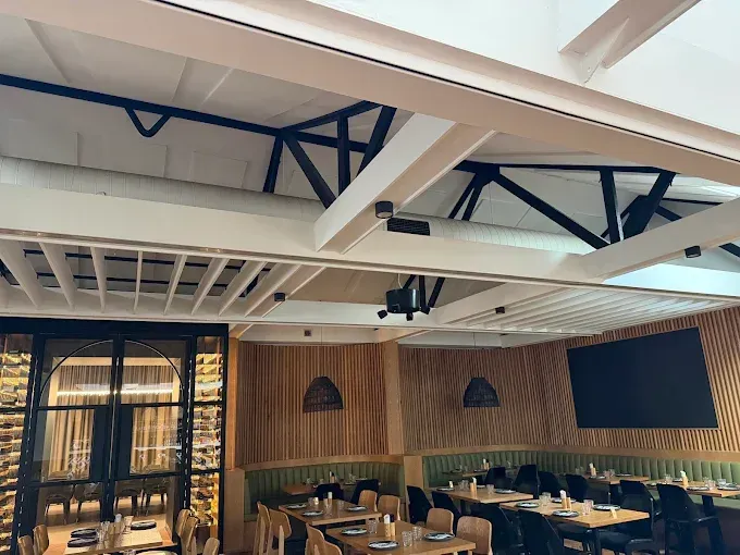 Modern restaurant dining area with wooden tables, chairs, and a high ceiling with exposed beams