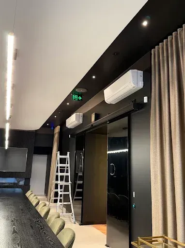 Modern conference room with chairs, ladder, wall-mounted AC, and dark doorway.