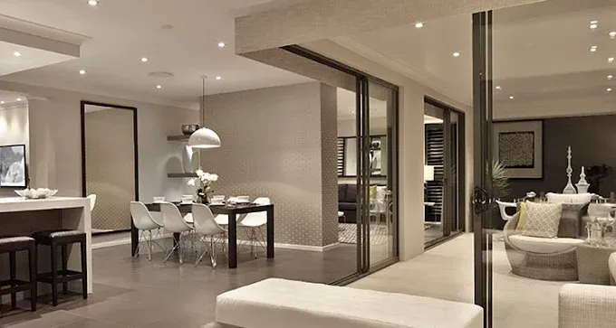 Modern open-plan living room and dining area with neutral decor, glass partitions, and warm recessed lighting