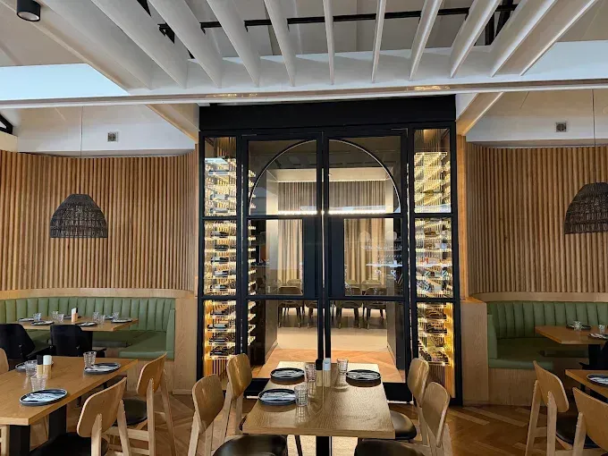 Modern restaurant interior with wooden booths, a central glass doorway, and tables set for dining