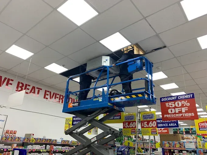 Blue scissor lift raised near a store ceiling with sale signs and merchandise aisles below