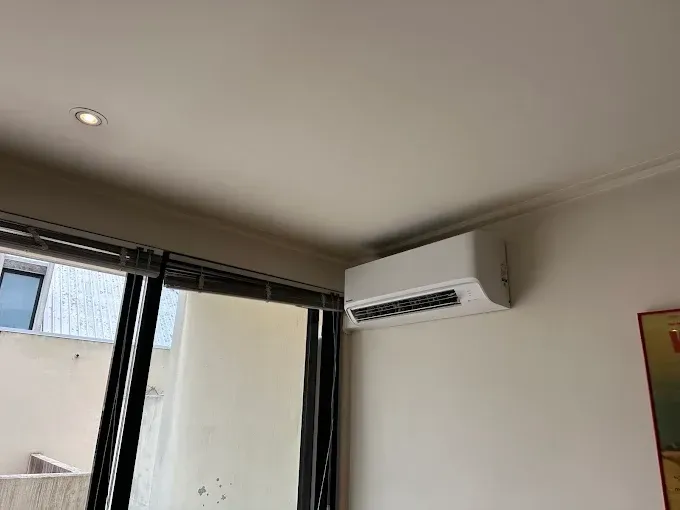 Corner of a room with a wall-mounted air conditioner above a window and curtains