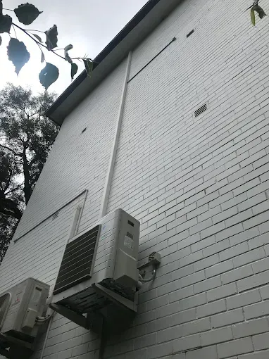 White brick building wall with two outdoor air-conditioning units and tree branches overhead