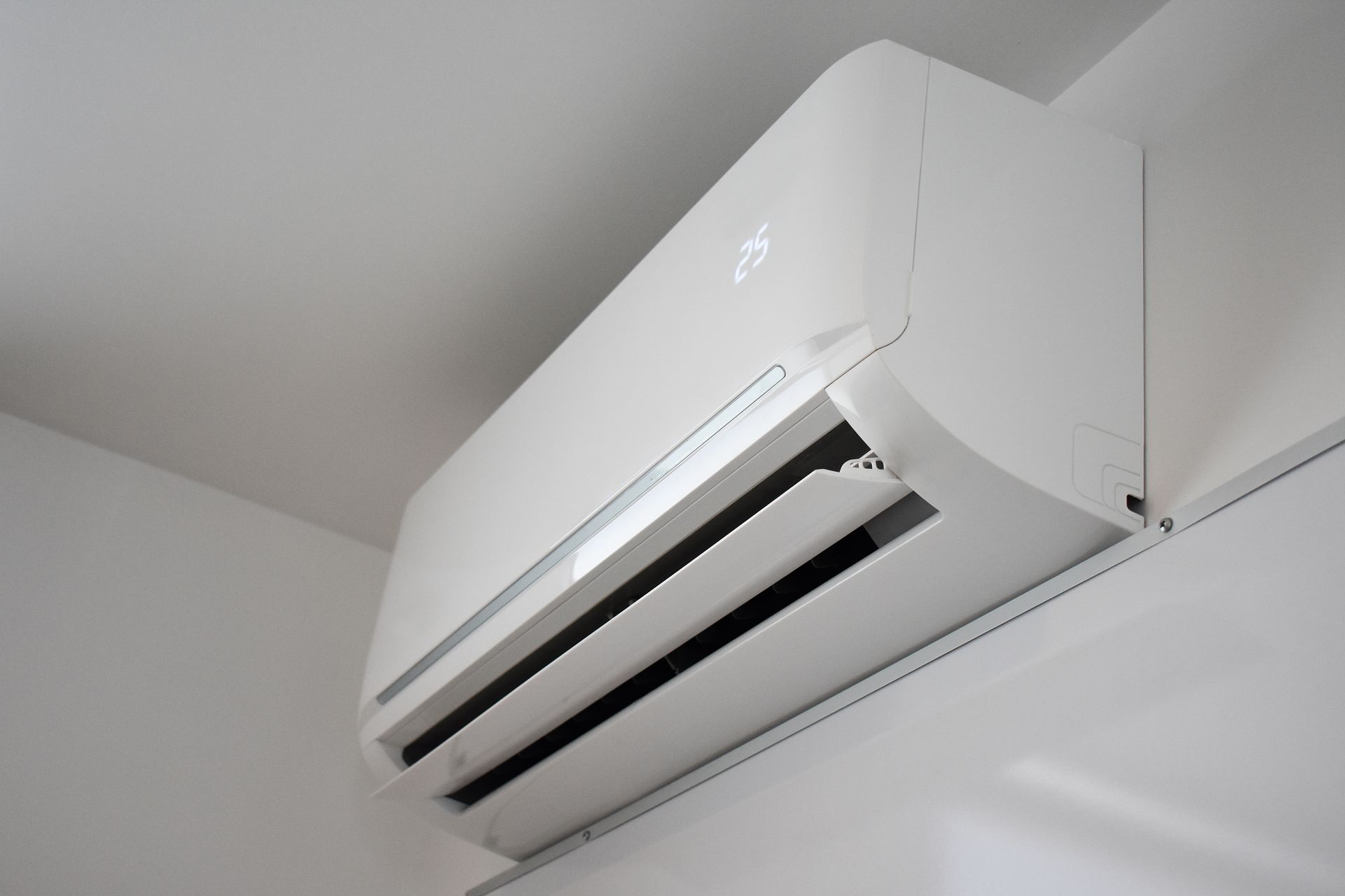 White wall-mounted split air conditioner near the ceiling in a room White wall-mounted split air conditioner near the ceiling in a room
