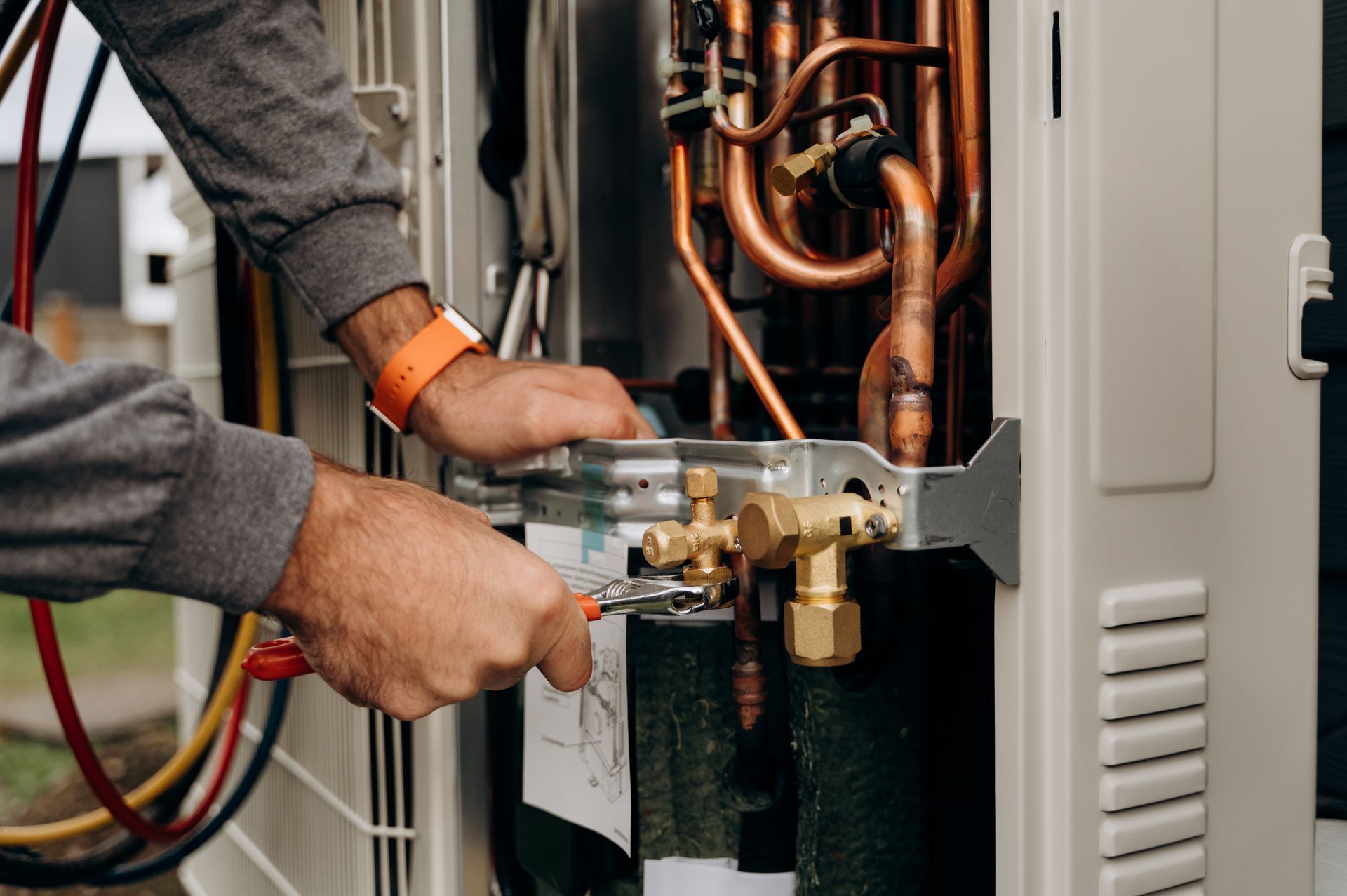 Technician adjusting copper piping inside an open HVAC unit with tools. Technician adjusting copper piping inside an open HVAC unit with tools.