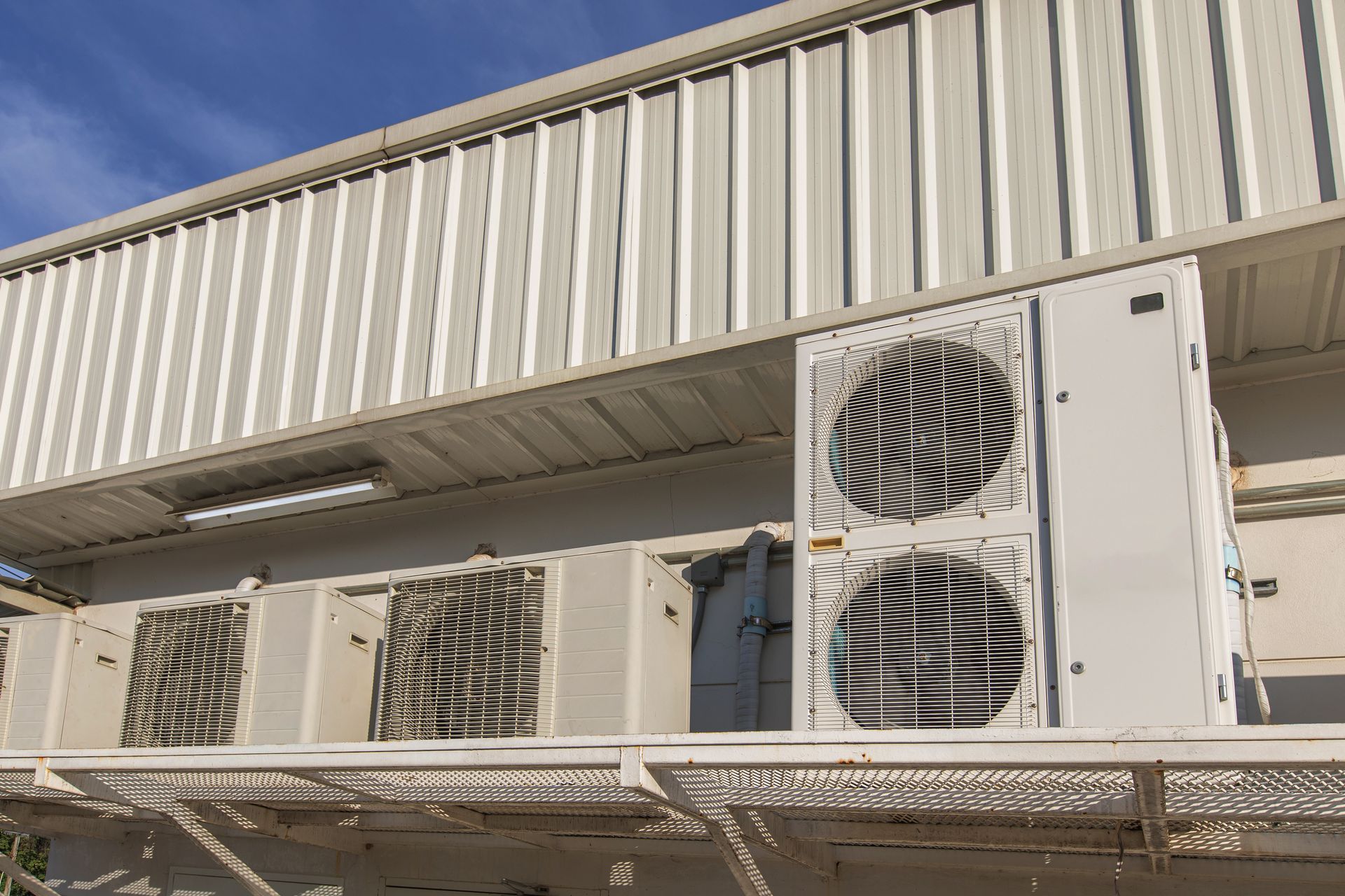 Outdoor air conditioning units mounted on a building wall under a metal overhang Outdoor air conditioning units mounted on a building wall under a metal overhang