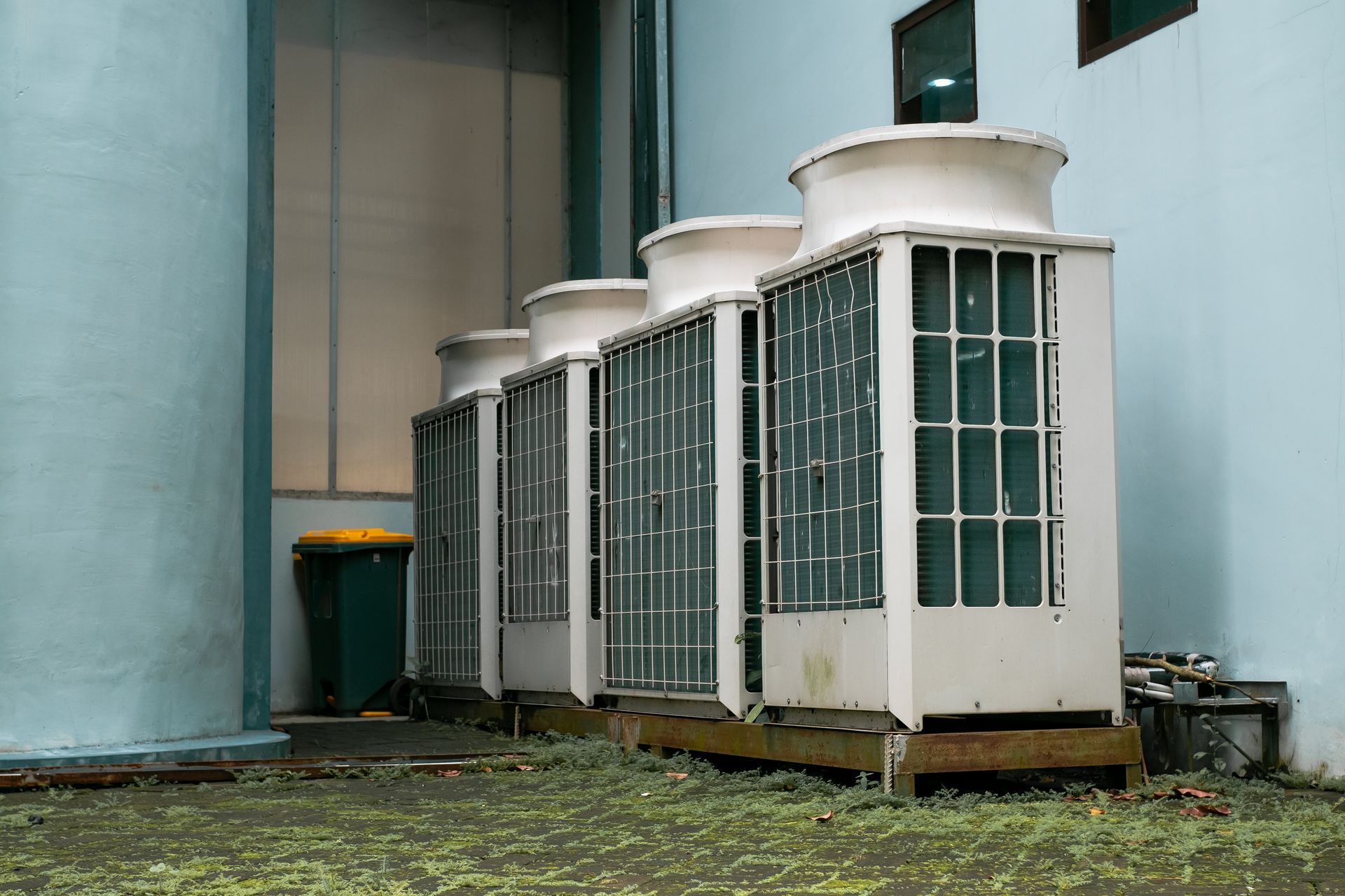Outdoor HVAC units beside a building wall, with large blue tanks and grassy ground.