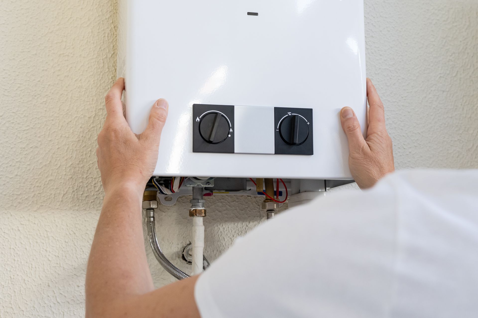 Person installing a white wall-mounted boiler, adjusting two black control knobs.