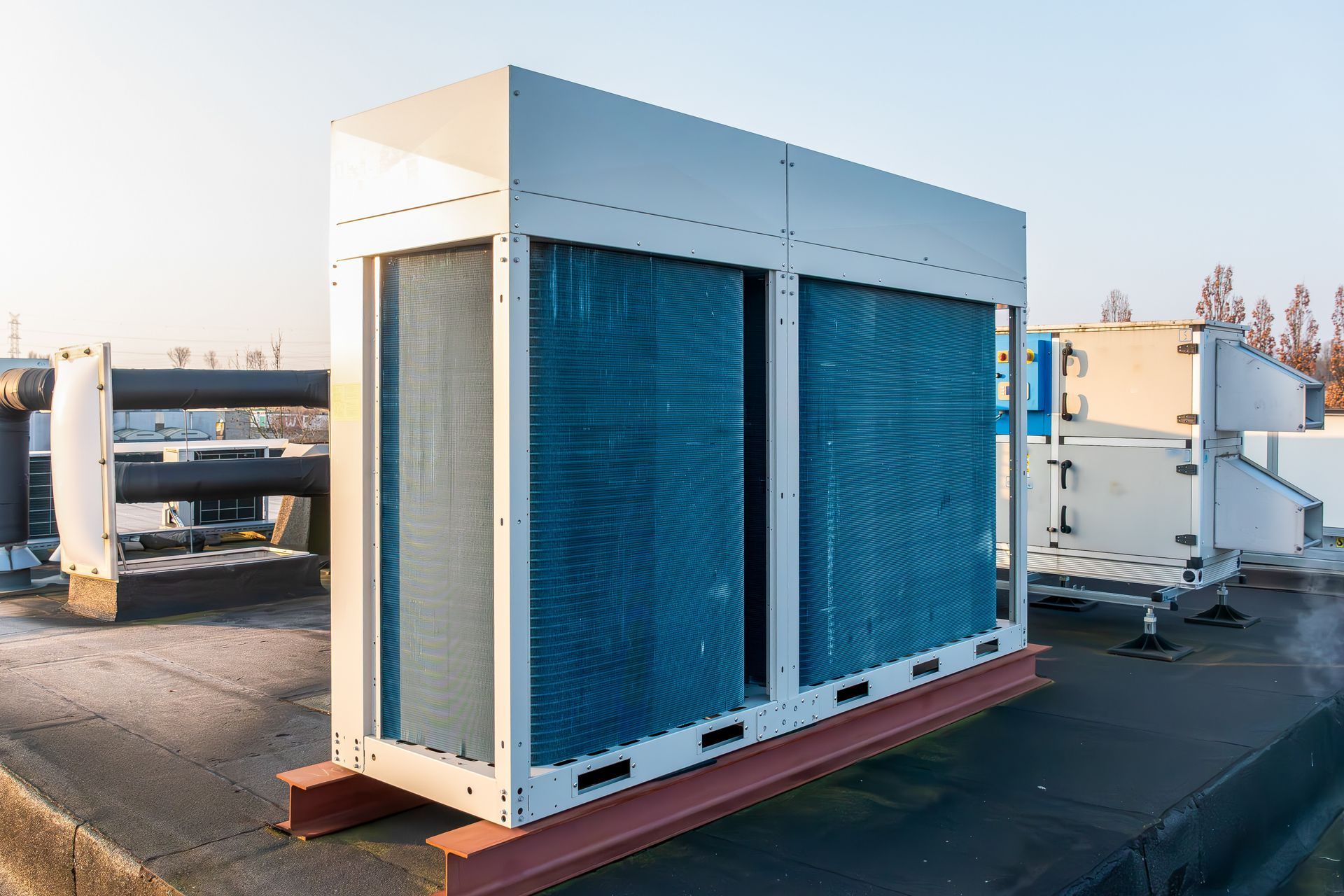 Large blue industrial HVAC unit on a rooftop, with pipes and equipment in the background Large blue industrial HVAC unit on a rooftop, with pipes and equipment in the background