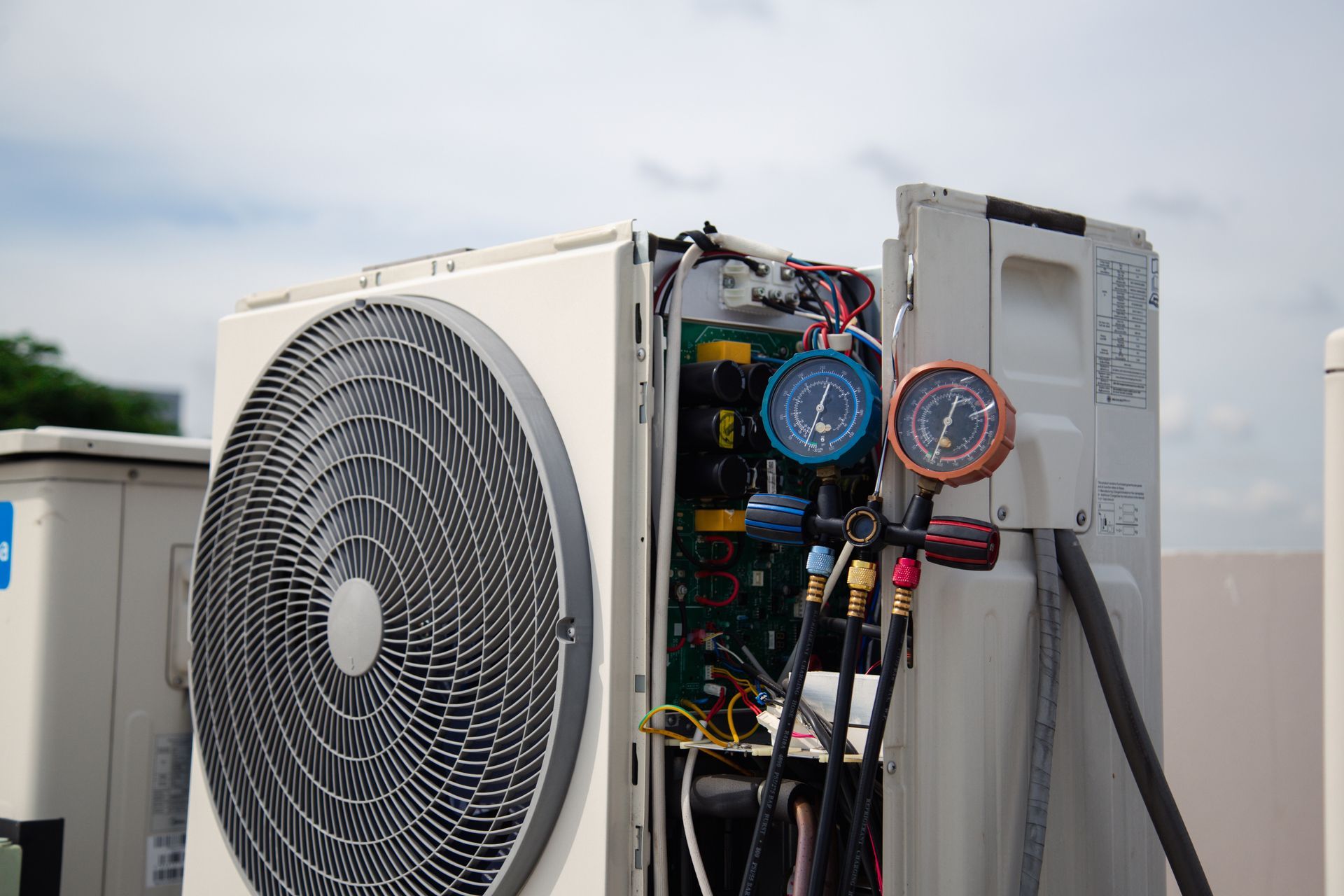 Open HVAC unit with exposed gauges and wiring beside a large fan outdoors Open HVAC unit with exposed gauges and wiring beside a large fan outdoors