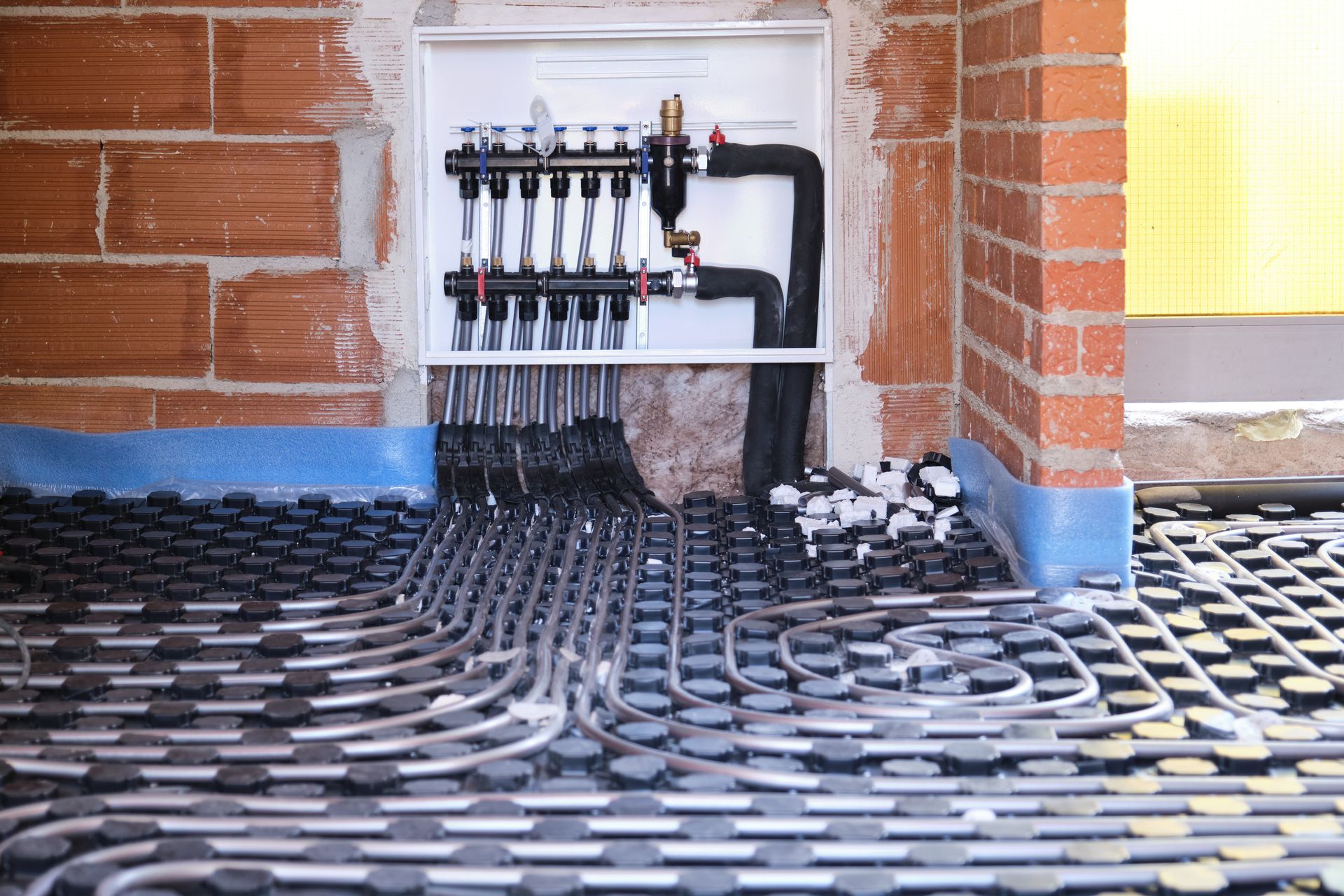 Floor heating pipes laid over insulation in an unfinished brick room under construction Floor heating pipes laid over insulation in an unfinished brick room under construction