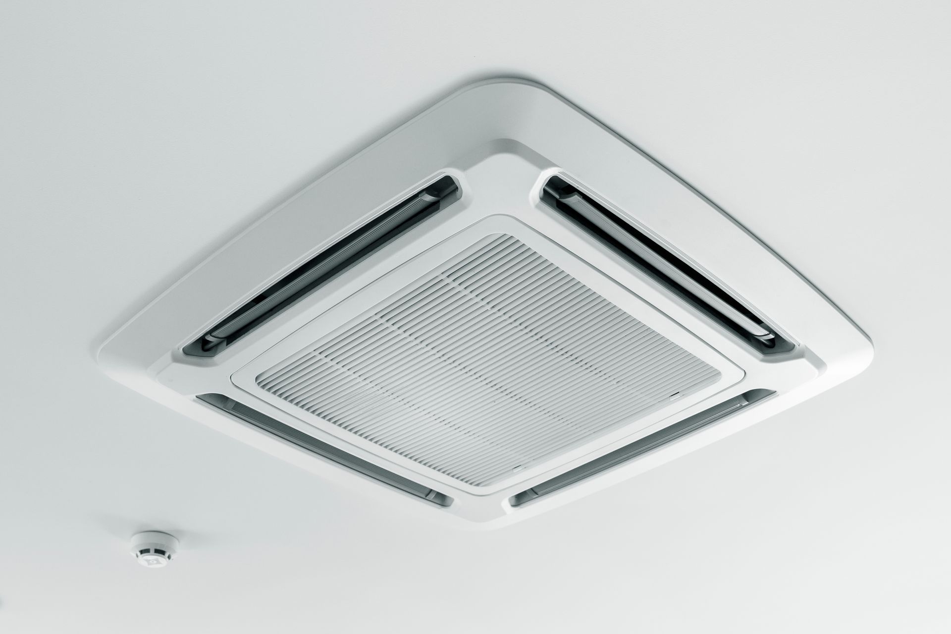 White ceiling-mounted air conditioner unit on a plain ceiling