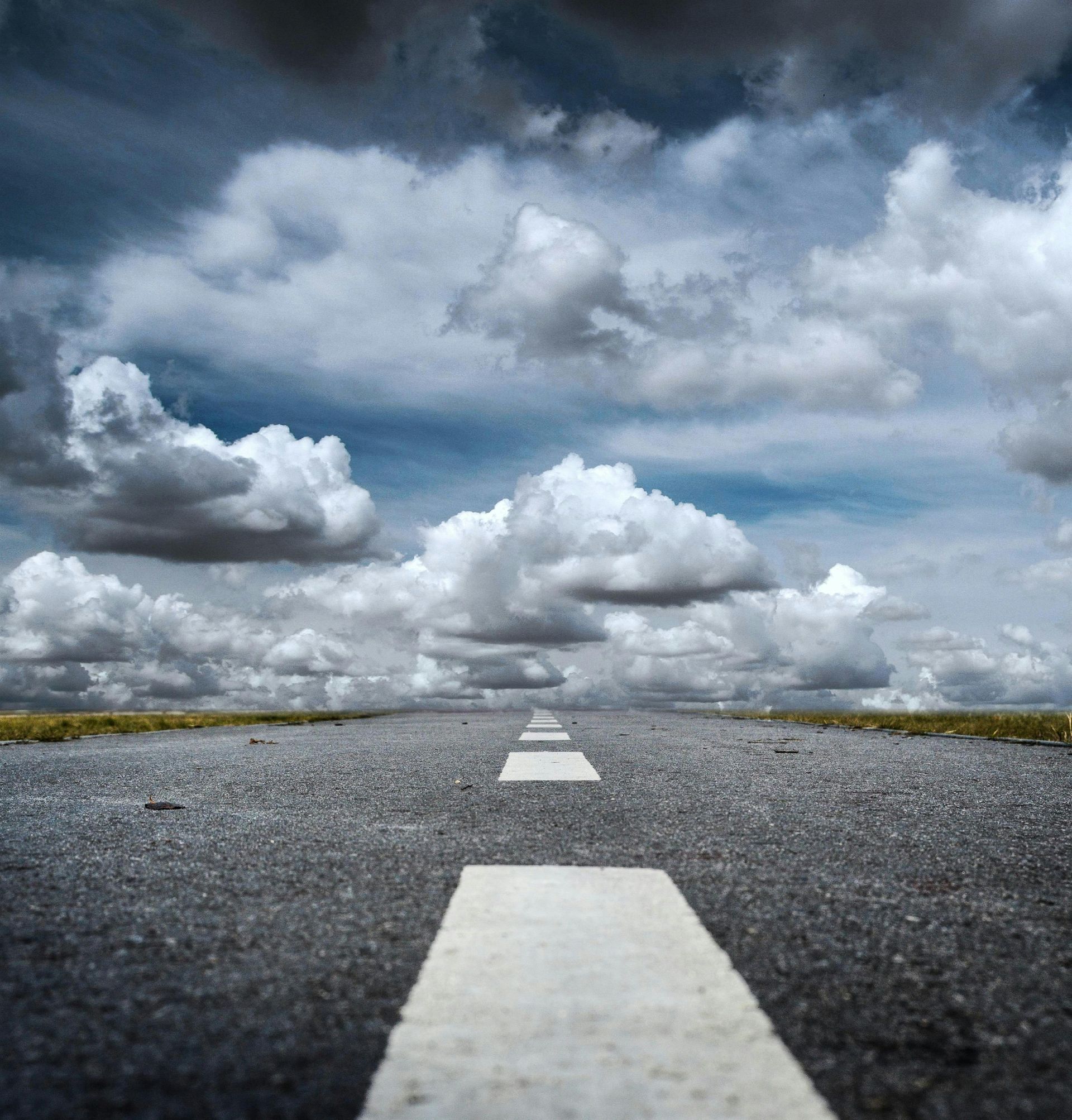 Road with white lines stretches towards cloudy sky.