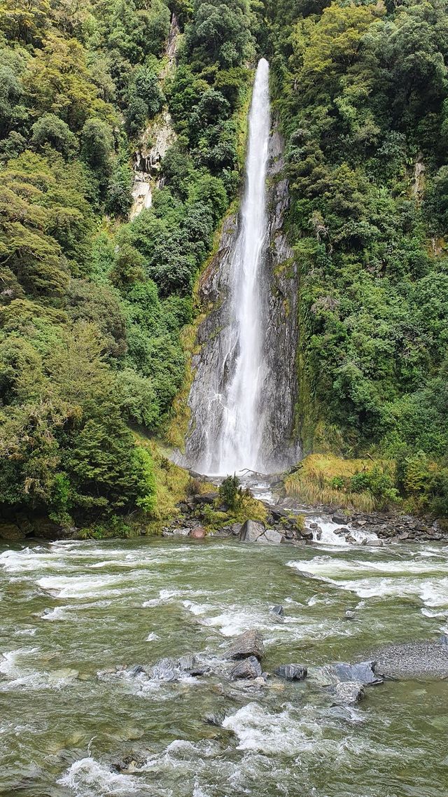 A tall waterfall above a rocky river in native bush