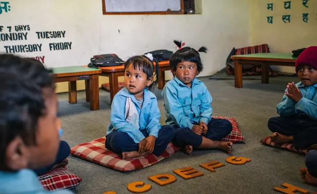 Young children sitting on cushions in a bright classroom