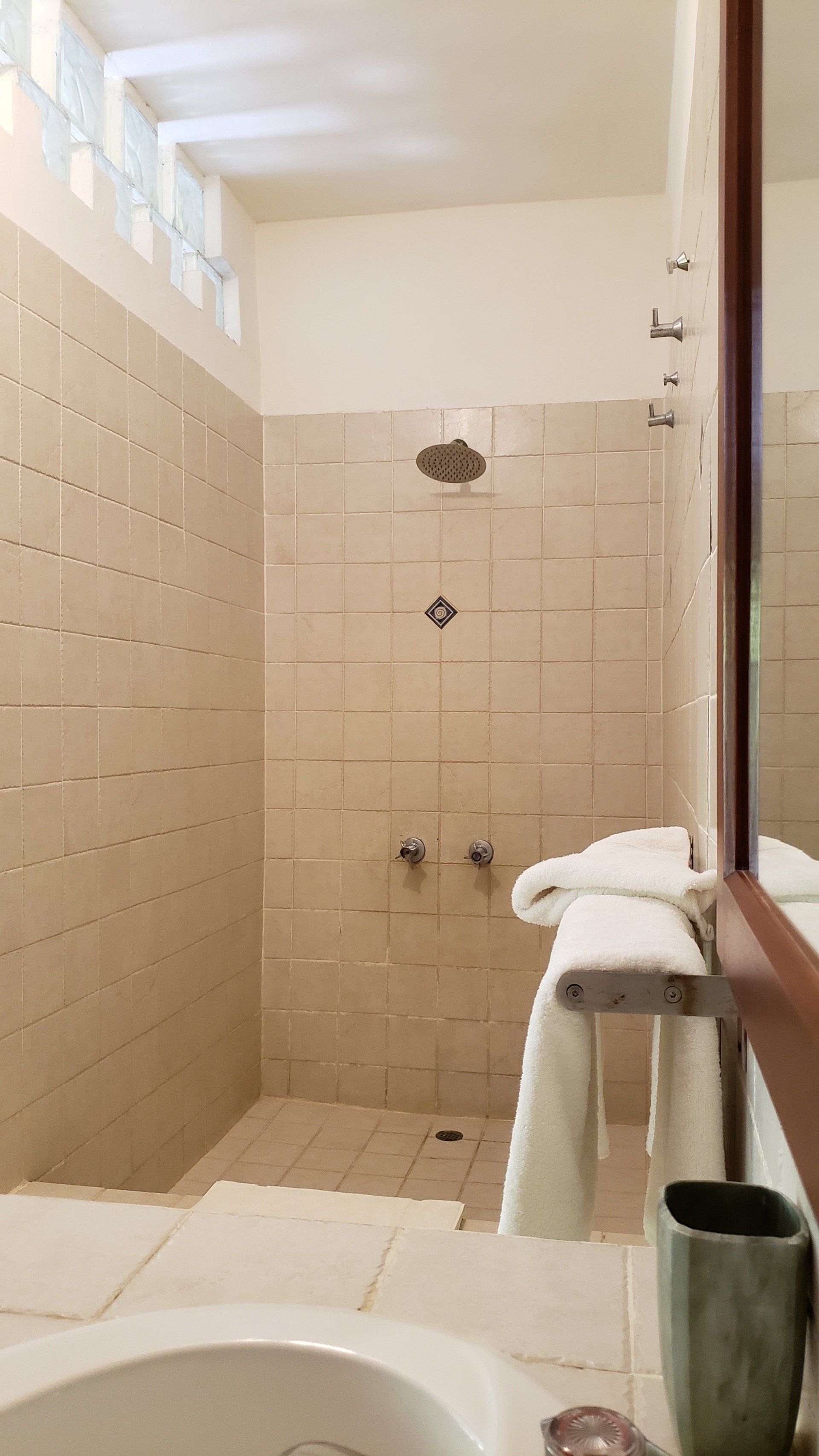 Shower with beige tile walls, glass block window, and towels hanging.