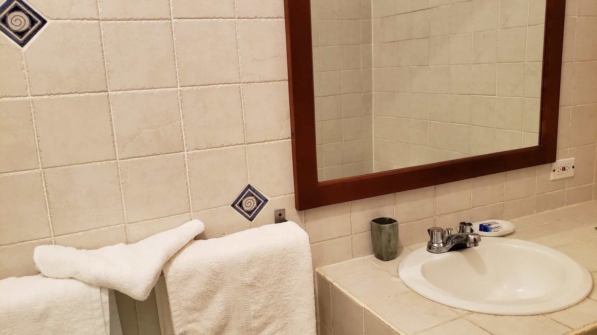 Bathroom with white tiled walls, towels, sink, and mirror. Brown mirror frame and blue accent tiles.