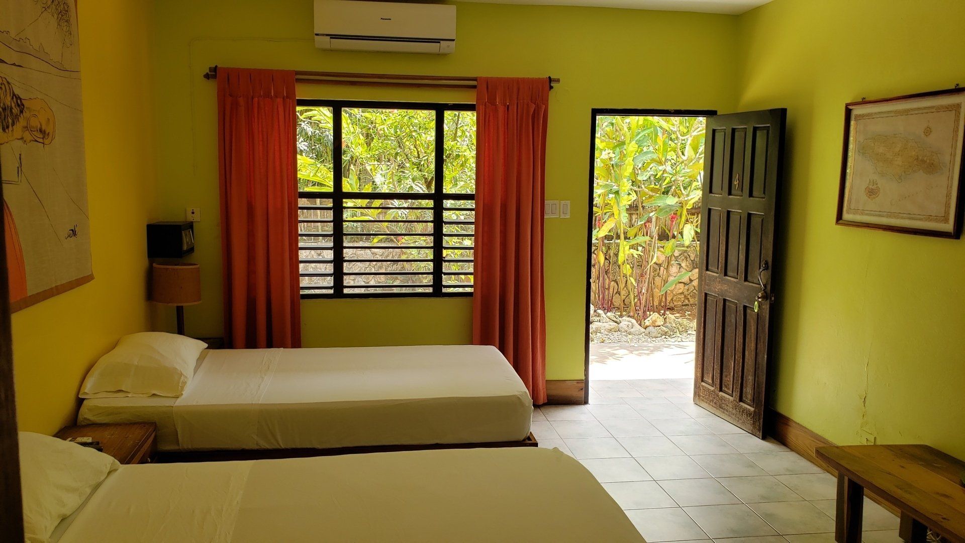 Two beds in a room with a window, door, orange curtains, and yellow walls.