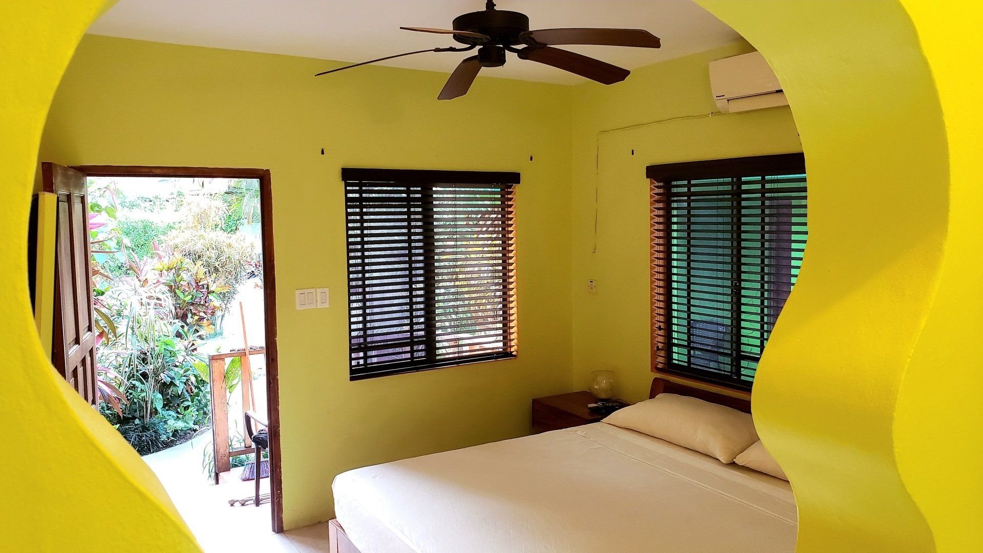 Bedroom with bed, open door to balcony, and two shuttered windows. Green walls, ceiling fan.