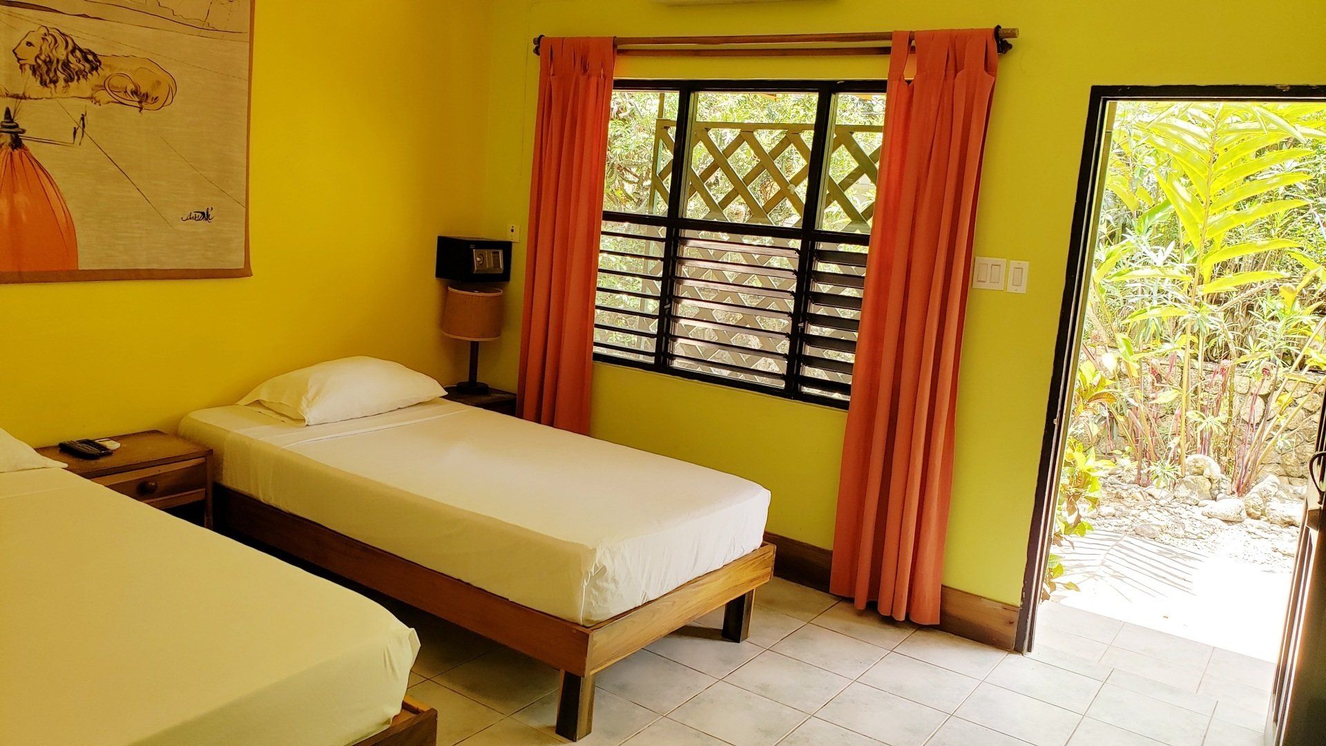 Yellow bedroom with two twin beds, window, orange curtains, open doorway to outside.