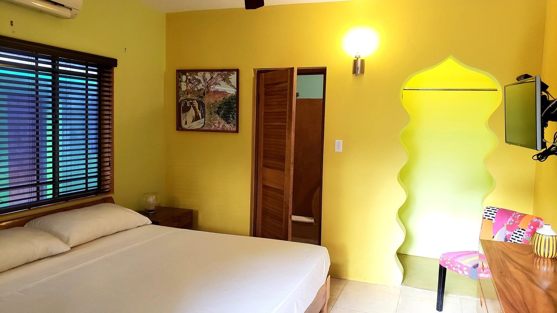 Bedroom with yellow walls, bed, window with blinds, and decorative arched doorway.