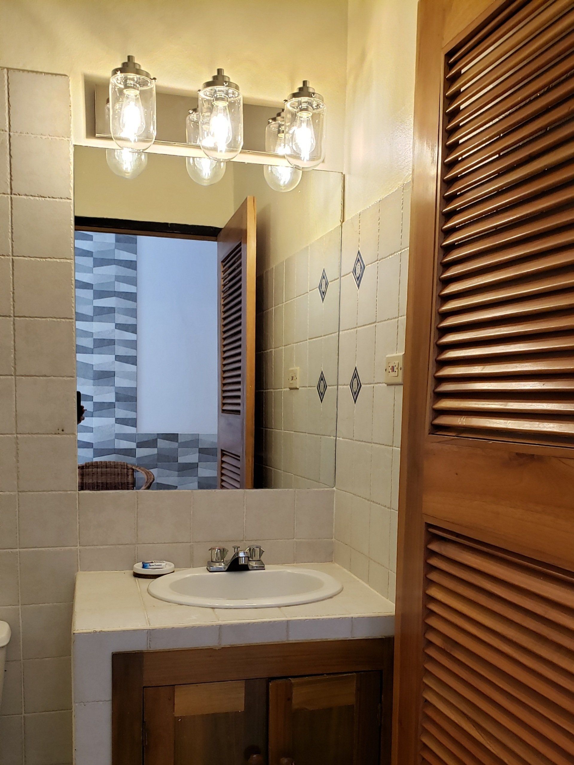 Bathroom with mirror, sink, and wood cabinet, with a view of a hallway.